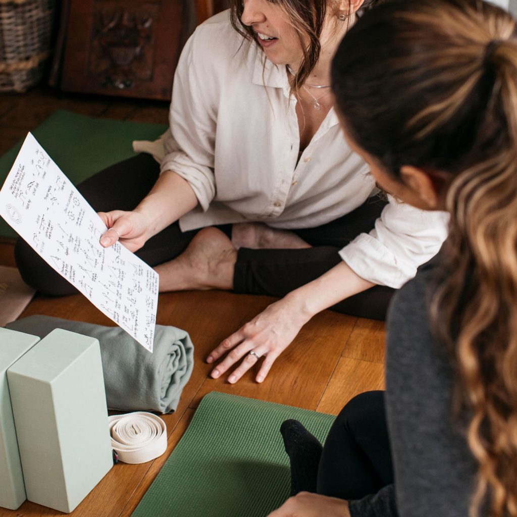 Andrea is sat on a yoga mat, showing a private client a yoga sequence to work through at home.